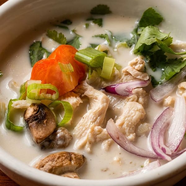 Close-up of a creamy soup with chicken, mushrooms, red onions, tomatoes, and green herbs.